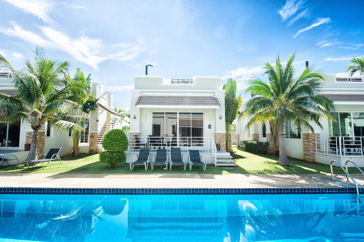 A modern hotel with a swimming pool, palm trees, and a well-maintained lawn.
