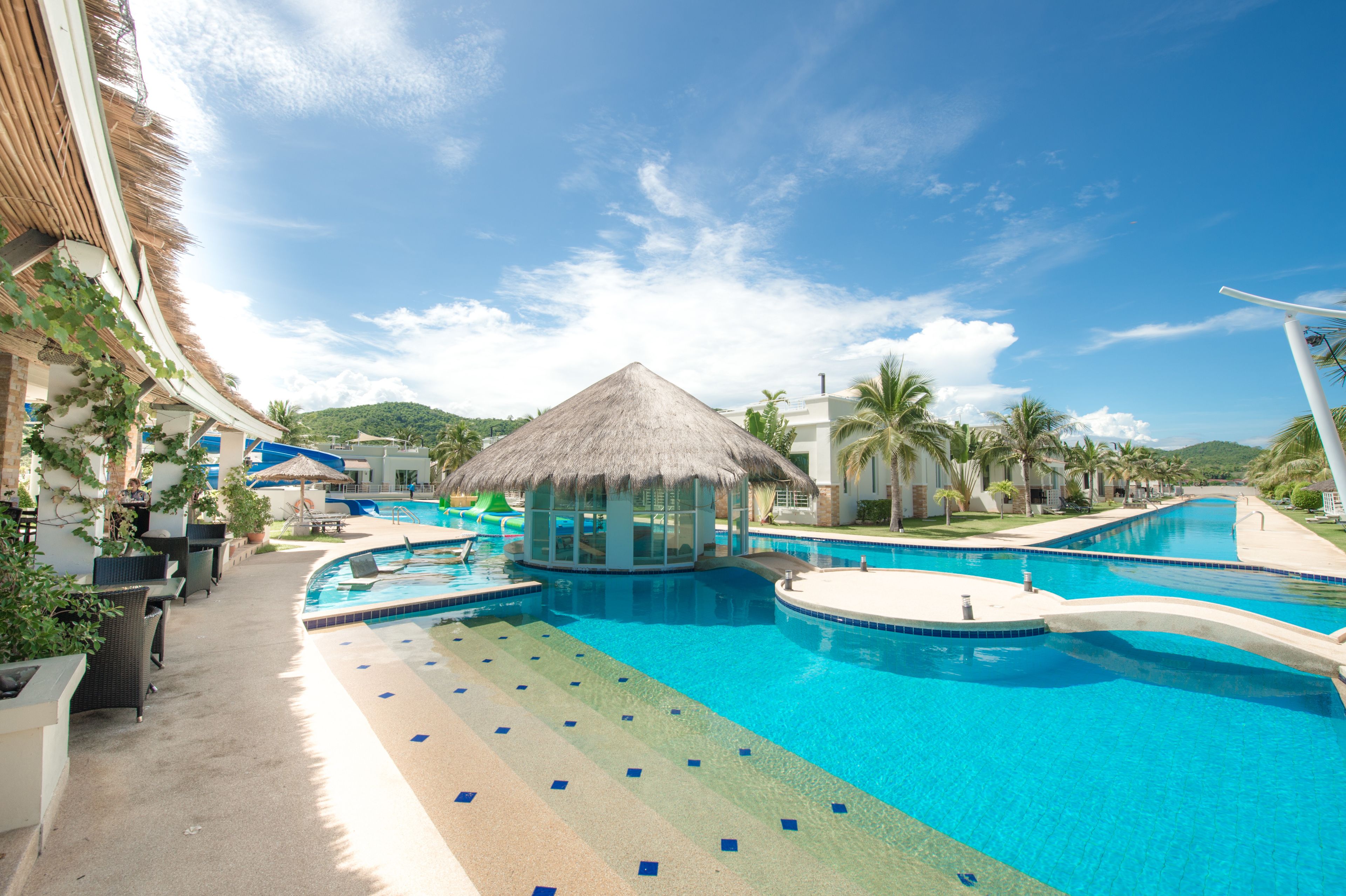 A resort pool area with a thatched-roof structure, lounge chairs, and a clear blue pool.