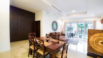 A modern dining area with a wooden table and chairs, a round mirror, and a view of the outdoors through large glass doors.