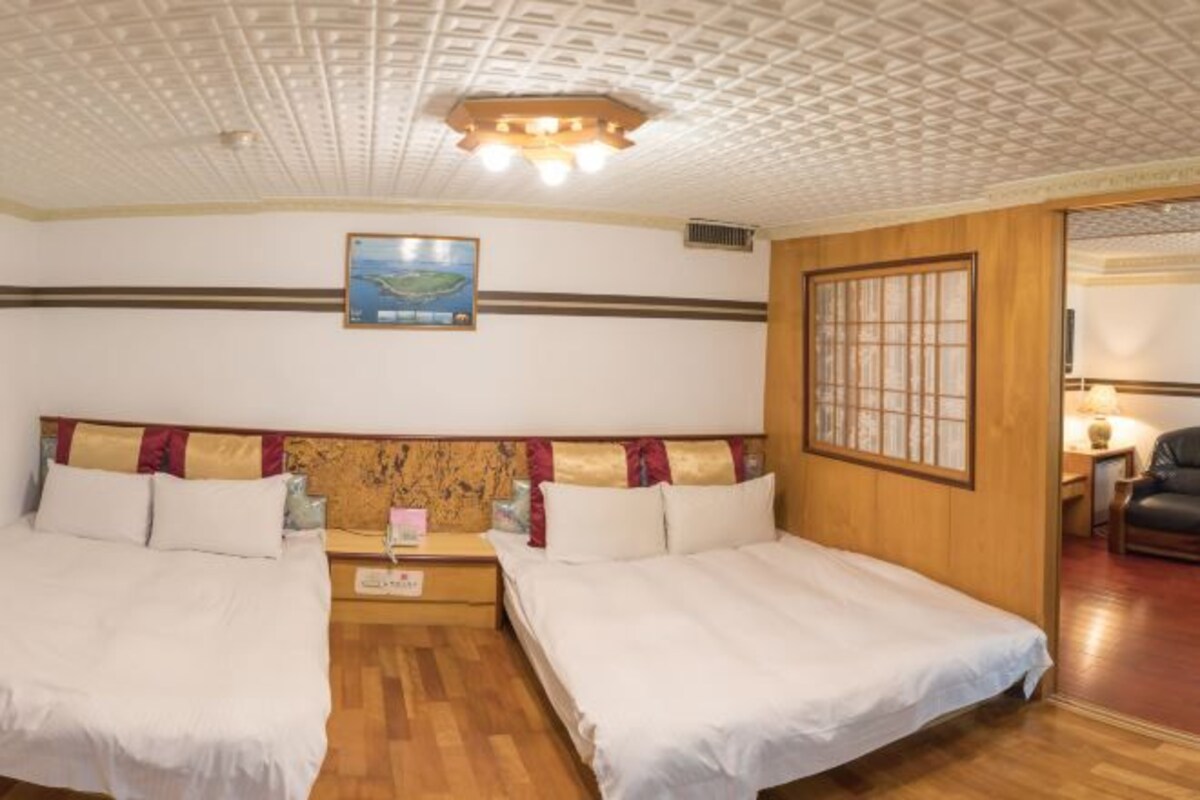 Ett hotellrum med två sängar, en sänggavel i trä, ett tak med ett rutmönster, en inramad tavla på väggen och en dörr i trä med en glaspanel.