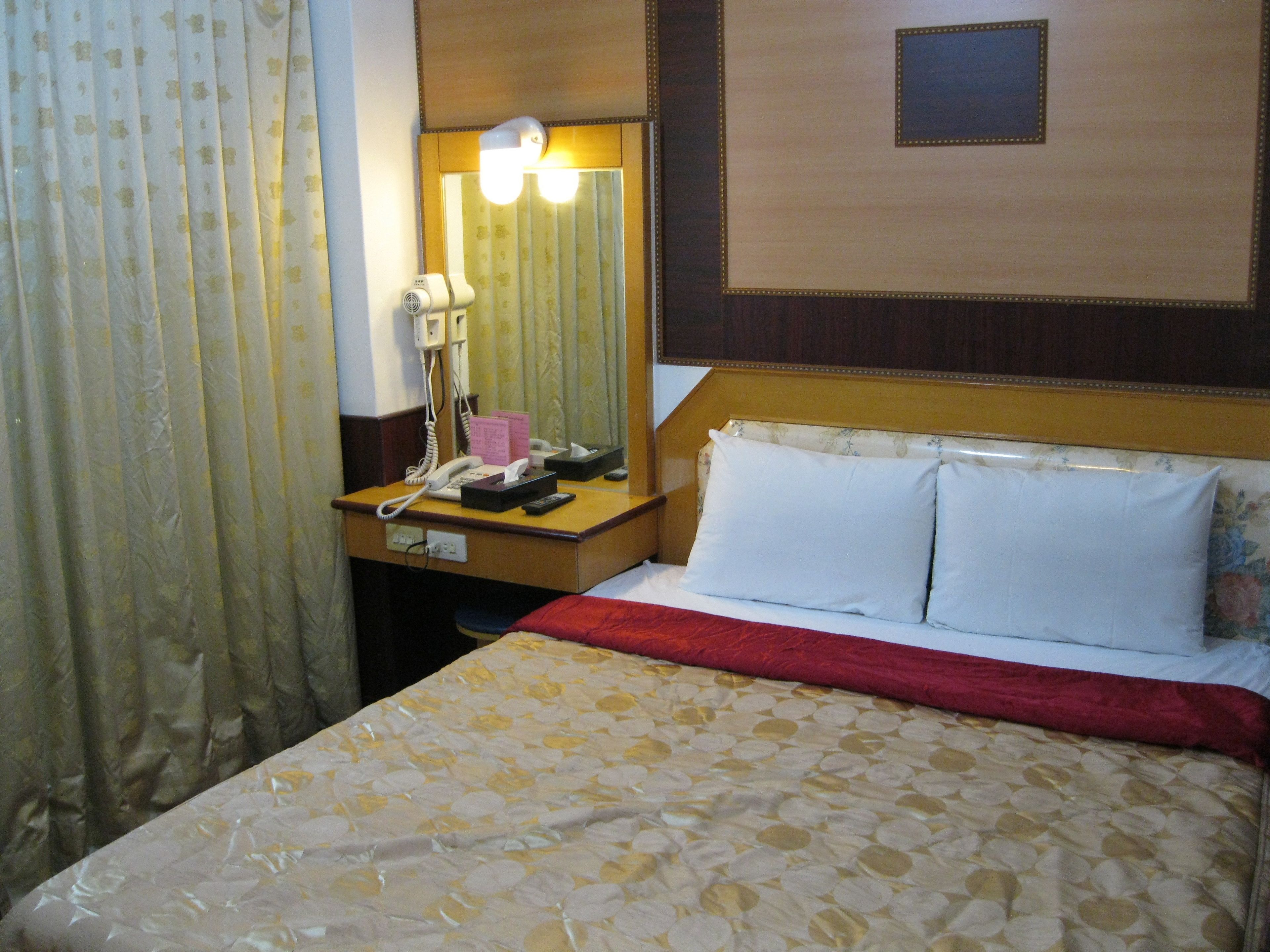 A hotel room with a bed, a bedside table with a telephone, a mirror, and a nightstand.
