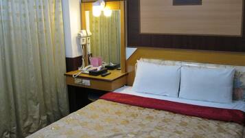 A hotel room with a bed, a bedside table with a telephone, a mirror, and a nightstand.