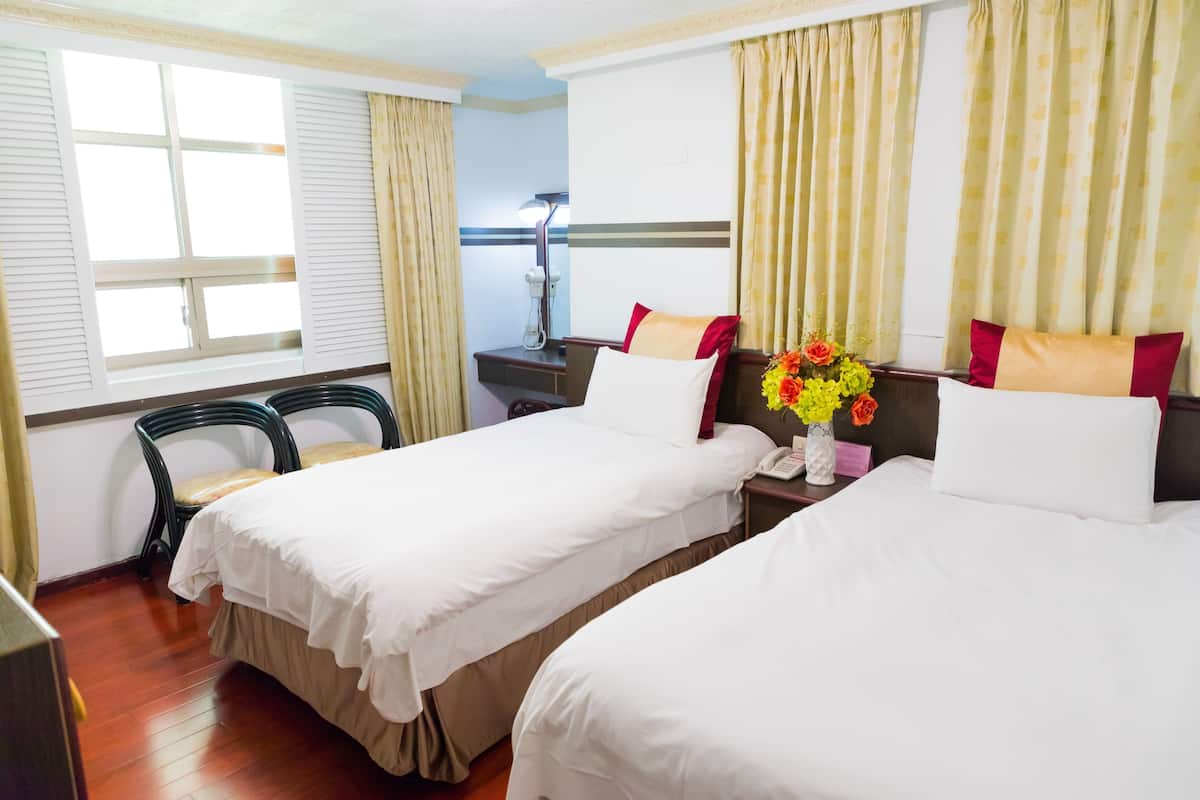 A hotel room with two beds, a desk, a chair, and a window with curtains.