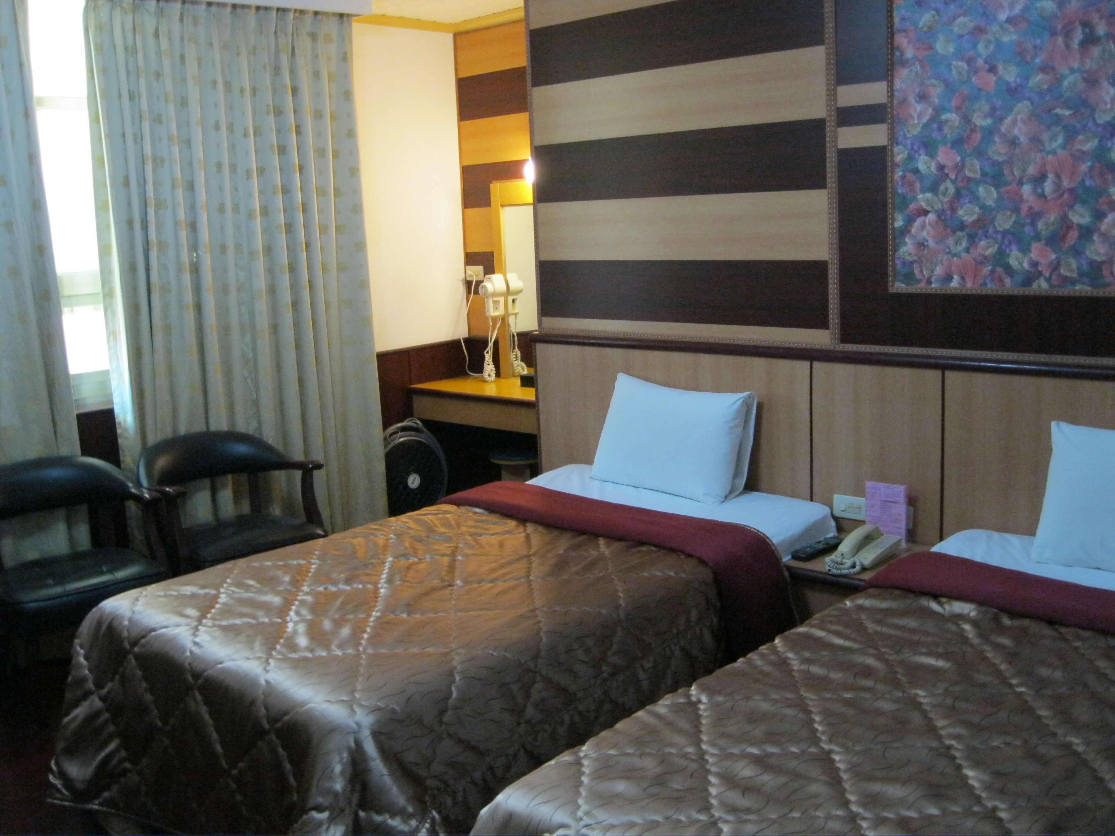 Ein Hotelzimmer mit zwei Betten, einem Schreibtisch, einem Stuhl und einem Fenster mit Vorhängen.
