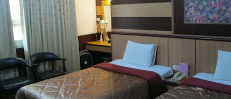 Ein Hotelzimmer mit zwei Betten, einem Schreibtisch, einem Stuhl und einem Fenster mit Vorhängen.