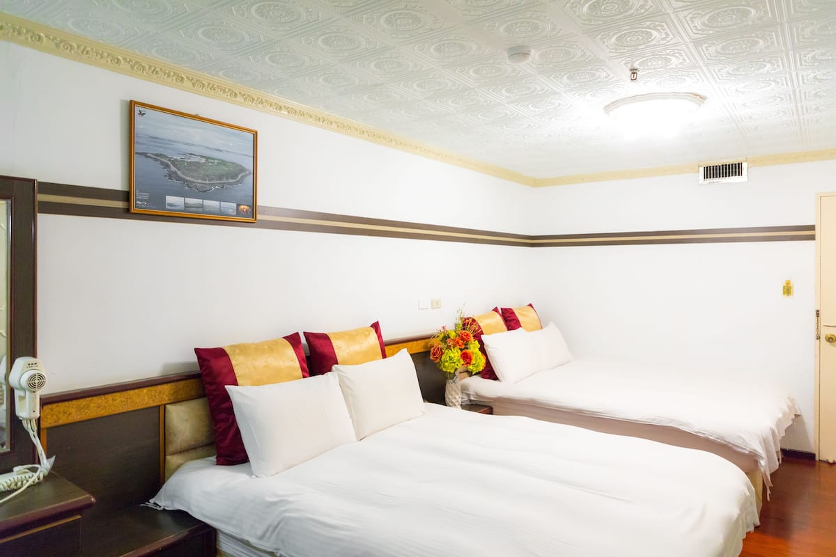 A hotel room with two beds, a nightstand with a phone, a decorative ceiling, and a framed picture on the wall.
