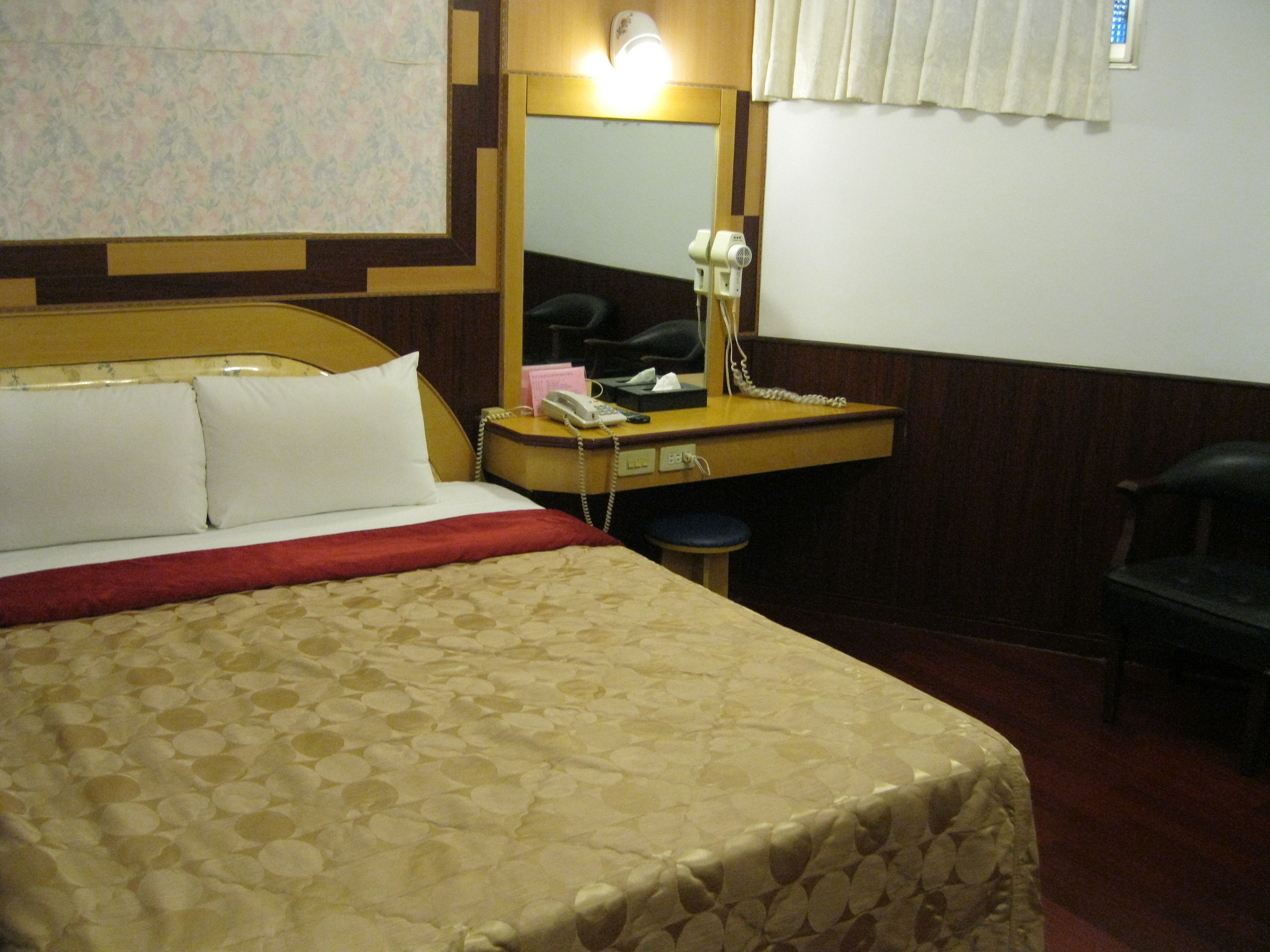 Una habitación de hotel con una cama, un escritorio con teléfono, un espejo y una silla.