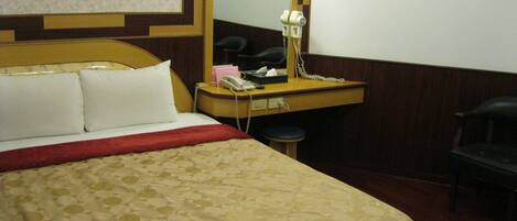 Una habitación de hotel con una cama, un escritorio con teléfono, un espejo y una silla.