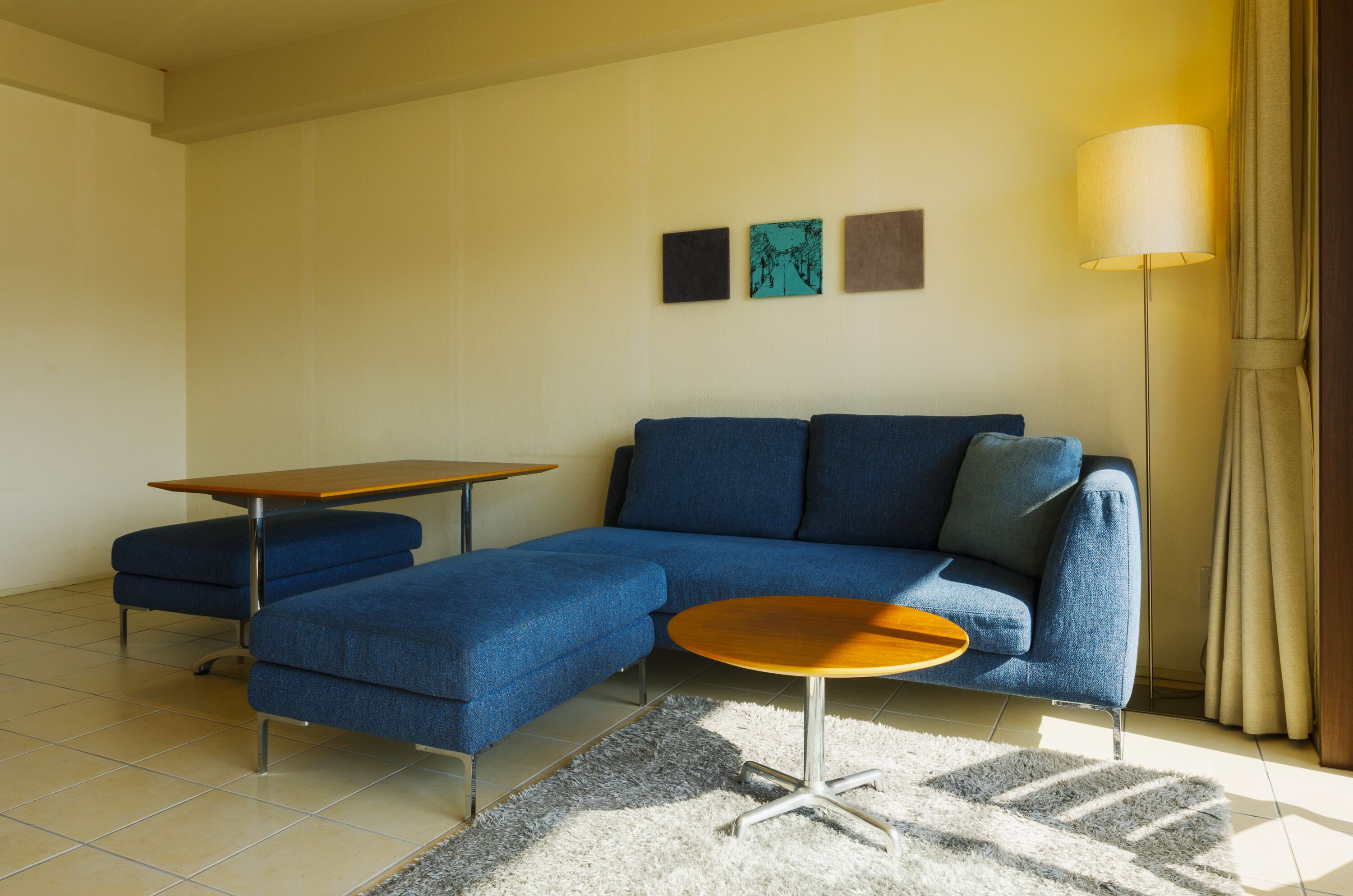 A modern living room with a blue sectional sofa, a wooden coffee table, and a small side table.