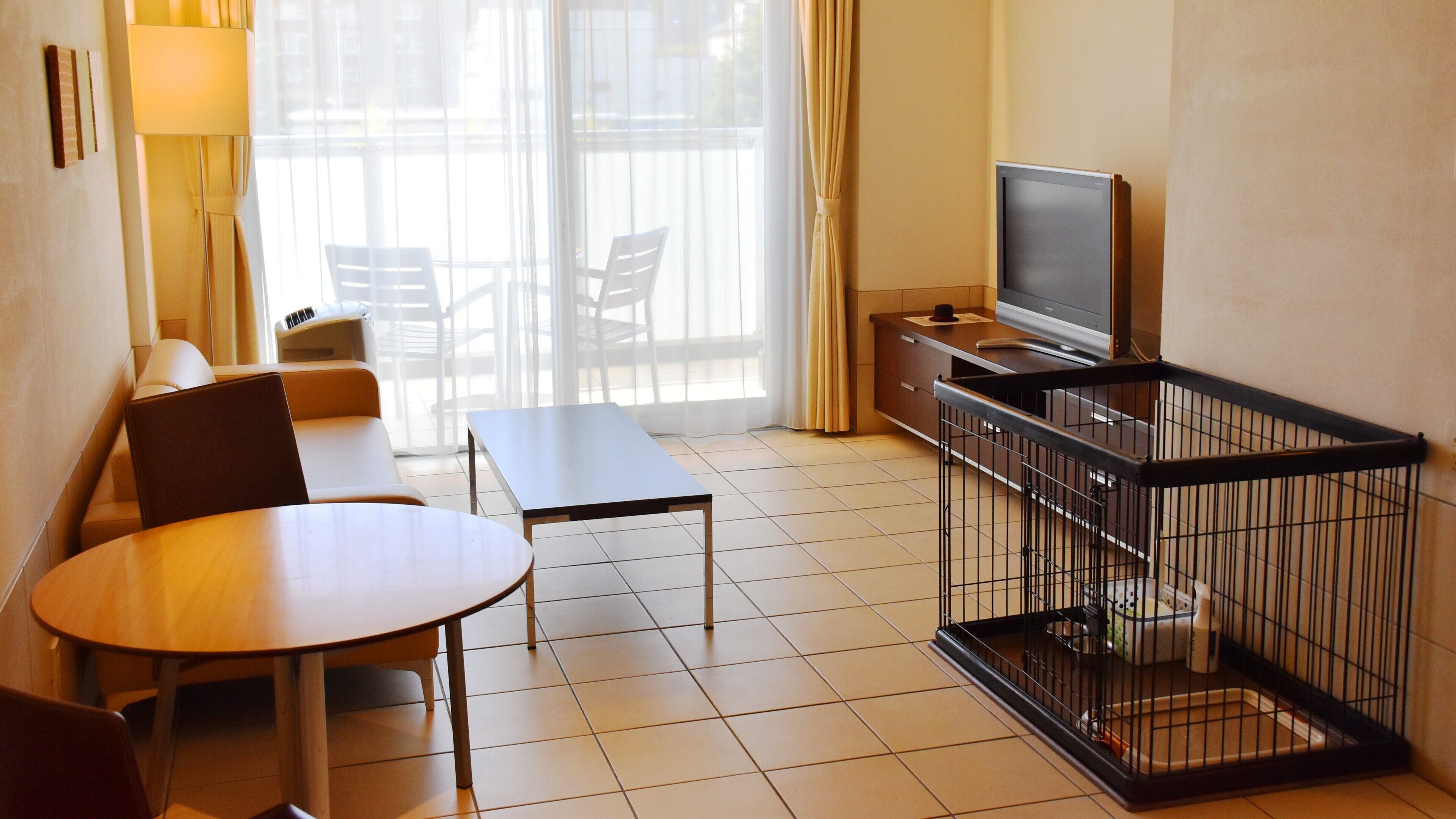 A hotel room with a sofa, a table, a TV, a cage, and a balcony with chairs.