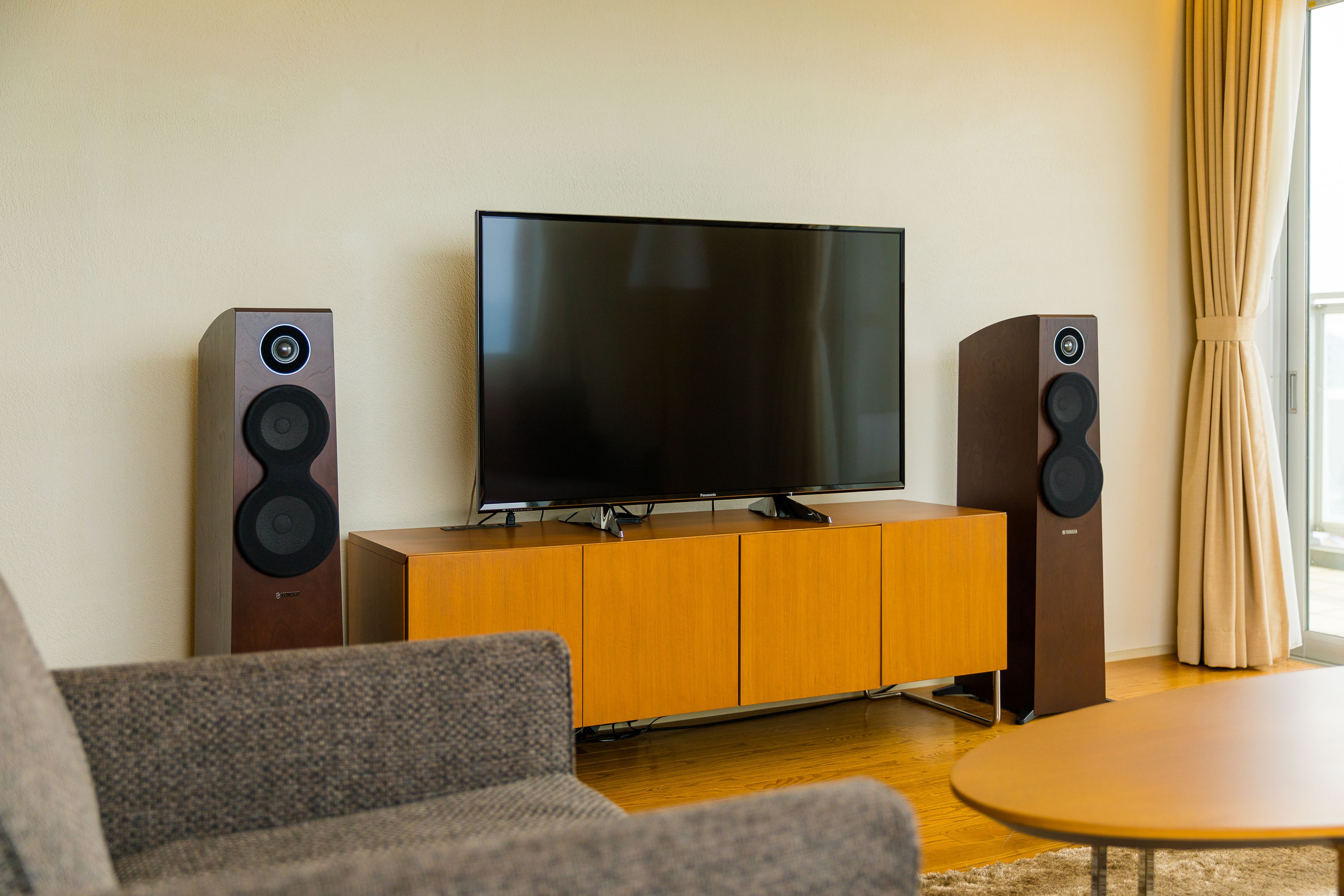 A modern living room with a flat-screen TV on a wooden cabinet, flanked by two floor-standing speakers.