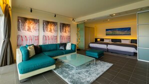Una habitación de hotel moderna con un sofá azul turquesa, una mesa de centro de vidrio y una cama con cabecera azul.