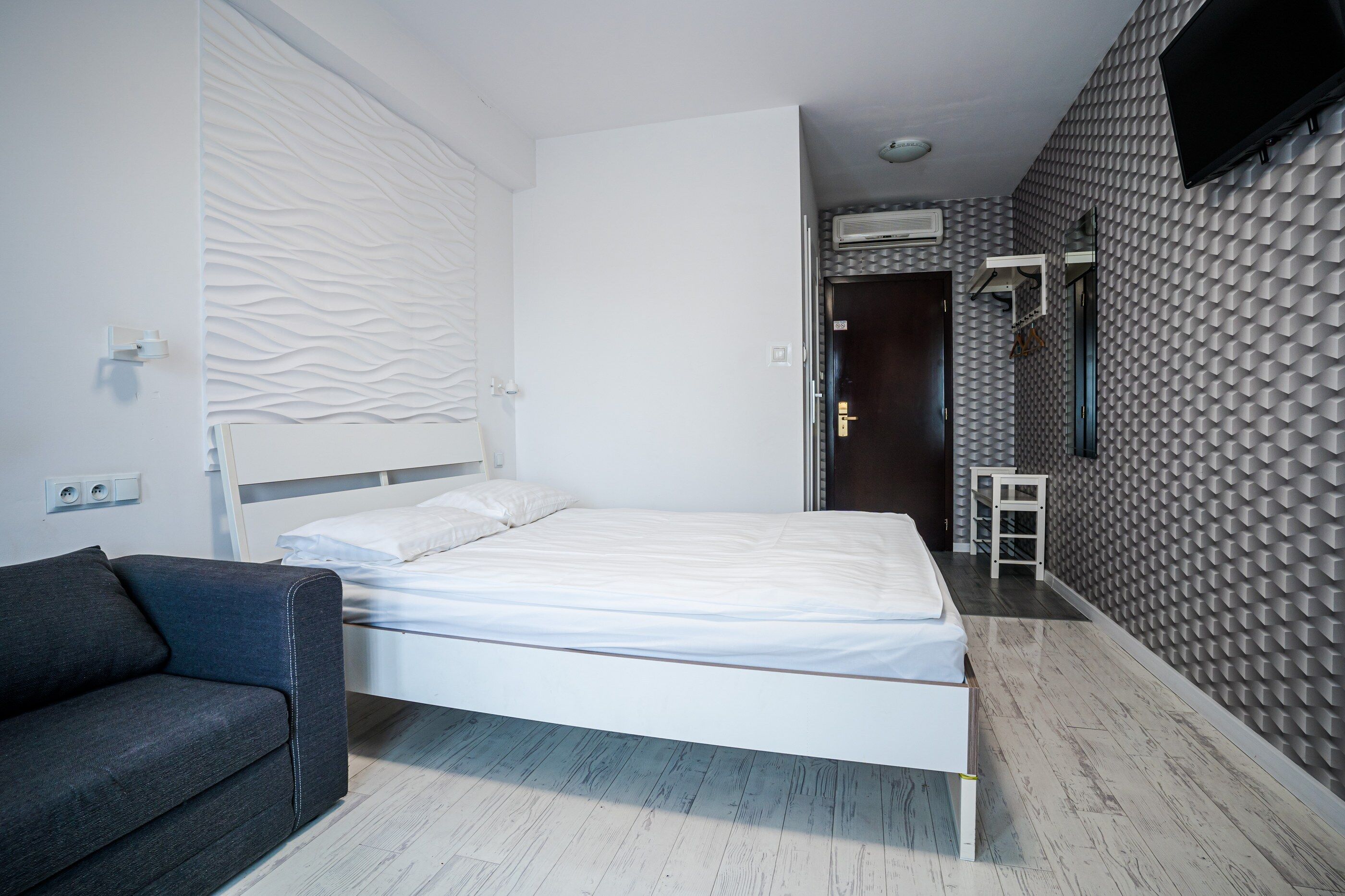 A modern bedroom with a bed, a sofa, a mirror, and a TV.