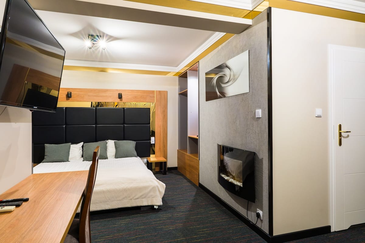 Una habitación de hotel con una cama, televisión, escritorio y chimenea.
