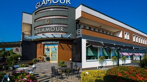 Un hotel llamado 'Glamour' con una fachada moderna, una zona de estar al aire libre y un restaurante visible llamado 'Restauracja'.