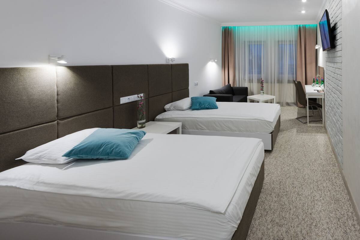 Habitación de hotel con dos camas, un escritorio, una silla y un televisor montado en la pared.
