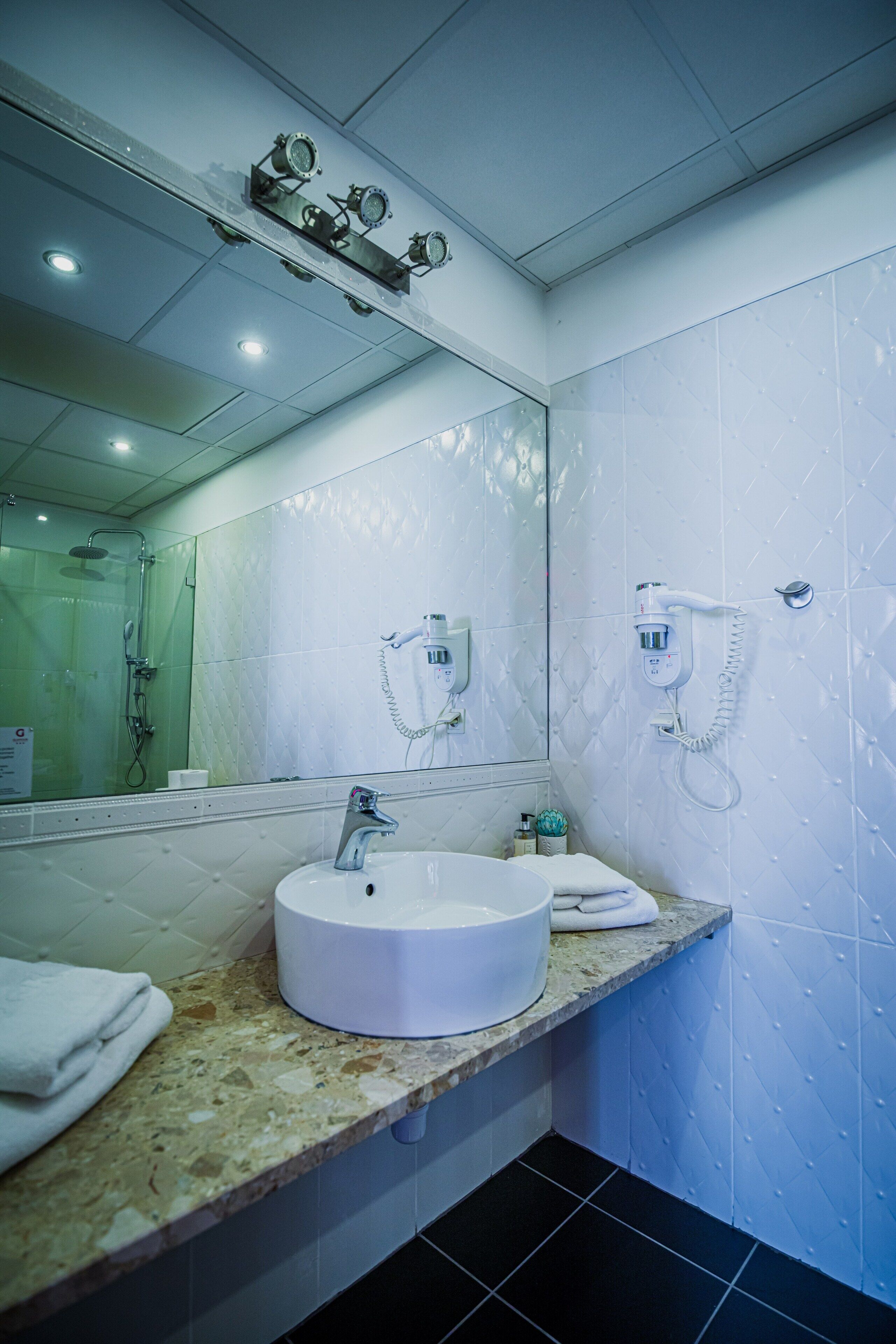 Een moderne badkamer met een grote spiegel, een rond wastafel en een handdouche.