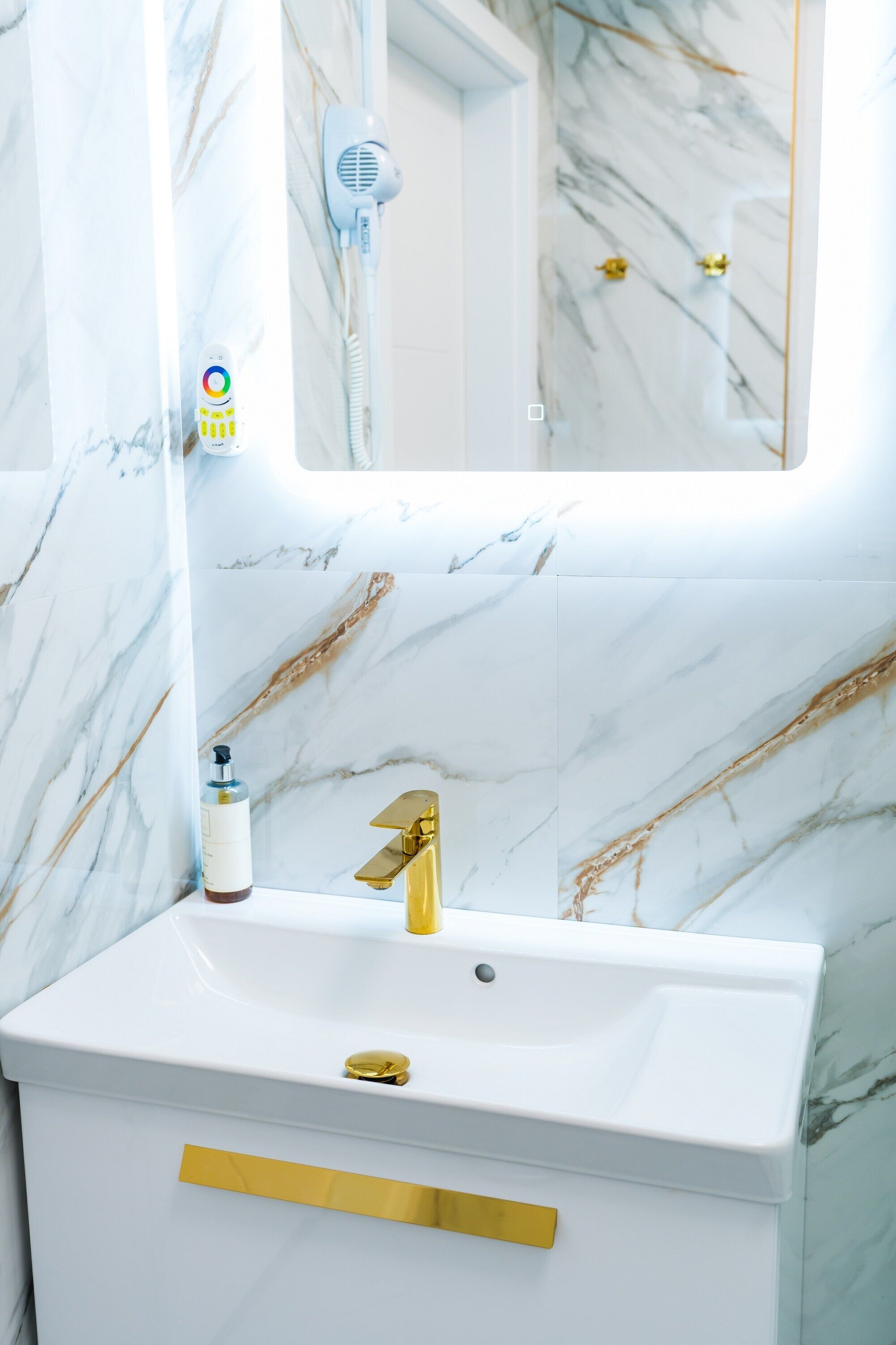 A bathroom with a white sink, gold faucet, and marble walls.