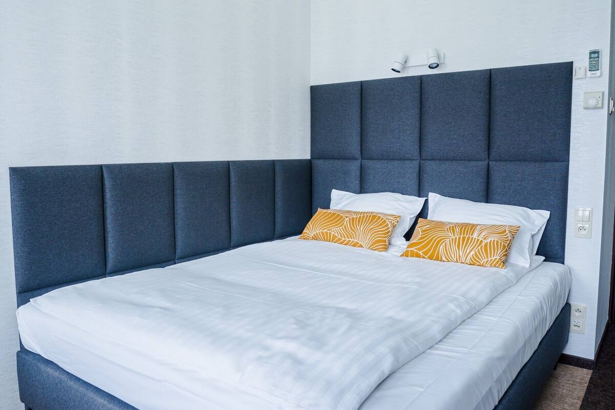 Una habitación de hotel moderna con una cama grande, cabecera oscura y una paleta de colores neutros.