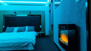 Una habitación de hotel moderna con una cama grande, una chimenea empotrada y un cabecero de madera.