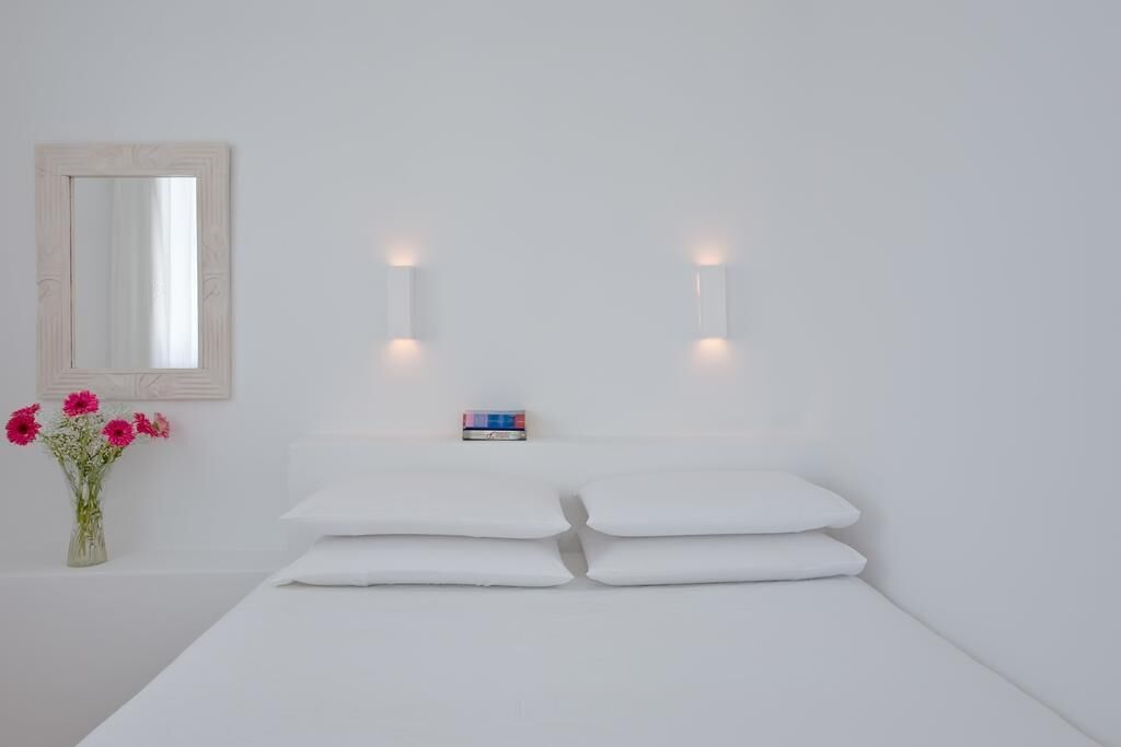 Une pièce minimaliste comprenant un lit, un miroir et des lampes fixées au mur.