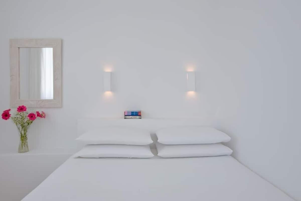 Una habitación minimalista con cama, espejo e iluminación en la pared.