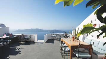 A terrace with a view of the sea, featuring a wooden table, chairs, and a sofa.