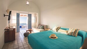 A bedroom with a large bed, a bedside table, a nightstand, and a view of the sea through an open door. - Remezzo Villas (Santorini)