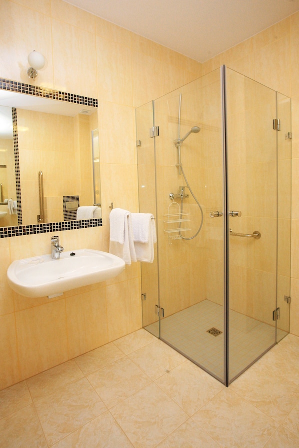 Un baño moderno con ducha envuelta en vidrio, un lavabo blanco y un espejo con un borde de azulejos blanco y negro.