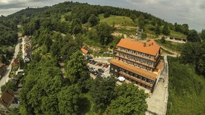 A multi-story building with a red-tiled roof, surrounded by lush greenery and a hilly landscape.