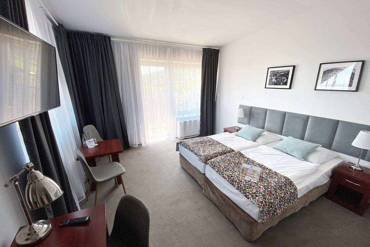 Een hotelkamer met een groot bed, een bureau met stoel, een televisie en een raam met gordijnen.