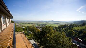 A view from a balcony overlooking a rural landscape with fields, trees, and distant hills.