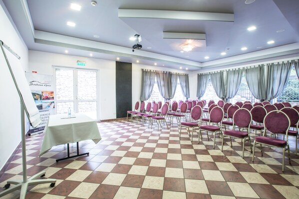 A conference room with a checkered floor, rows of purple chairs, a white table, and a projector on the ceiling. - Hotel Srebrna Góra (Stoszowice)