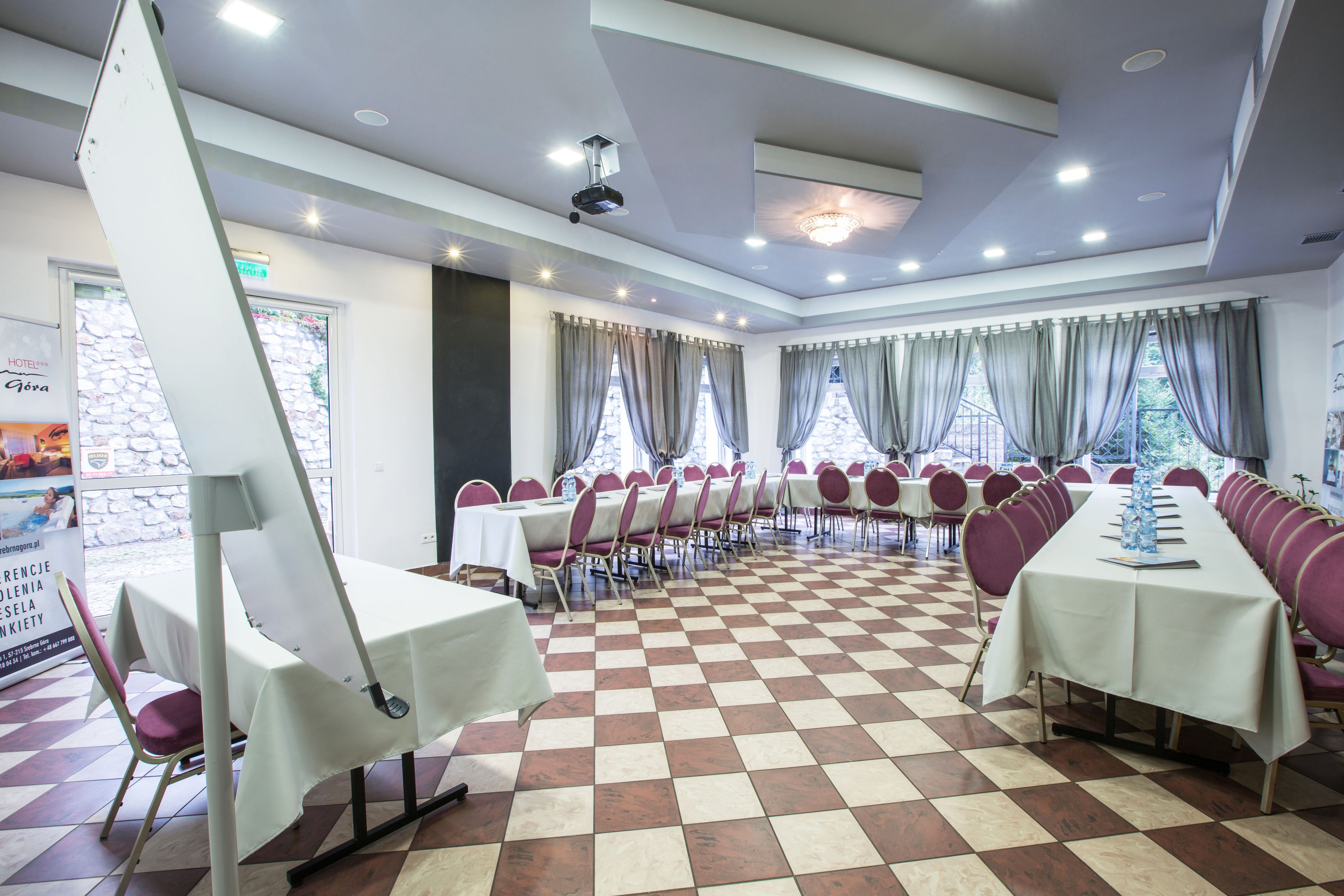 A conference room with checkered flooring, tables with white tablecloths, and chairs with purple cushions.