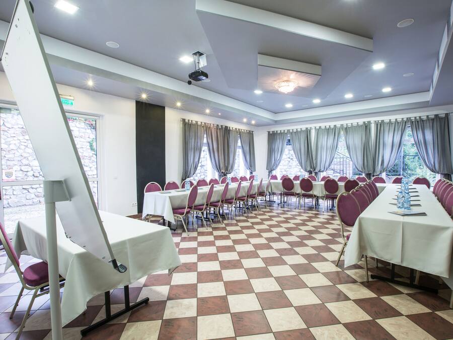 A conference room with checkered flooring, tables with white tablecloths, and chairs with purple cushions.
