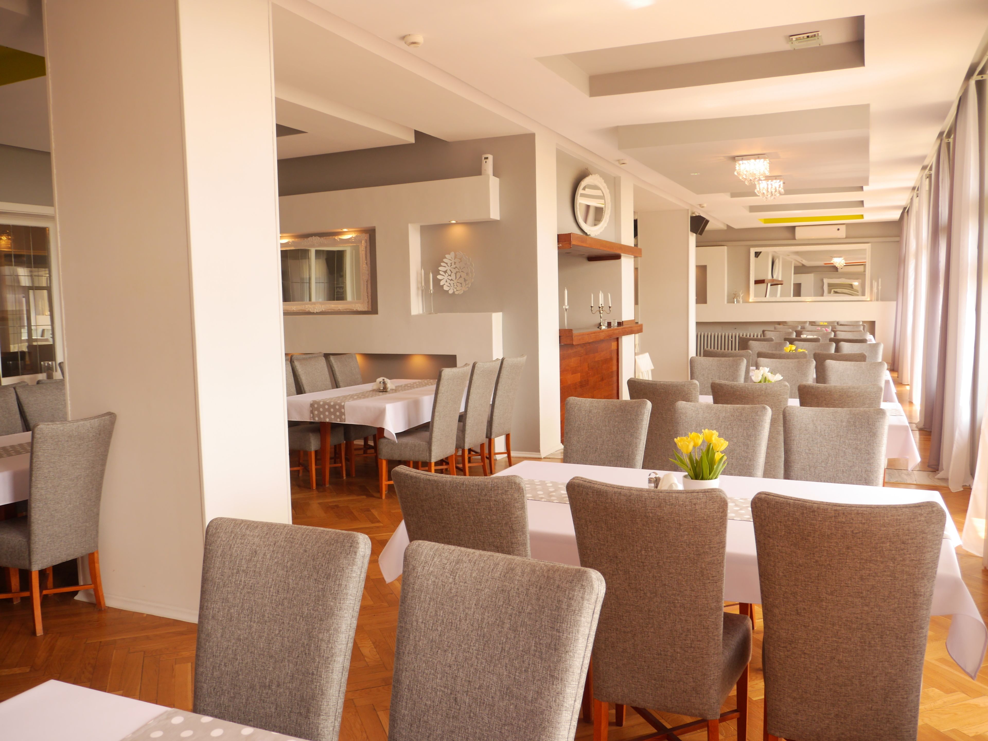 A modern dining area with grey upholstered chairs and white tablecloths.