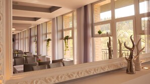 A hotel corridor with a mirrored wall, seating area, and large windows with curtains.