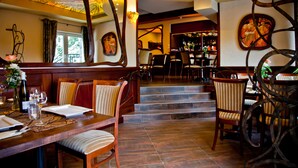 A restaurant with a bar area, wooden furniture, and a staircase leading to the bar.