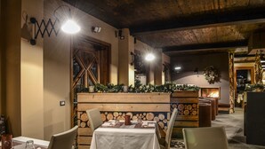 Un restaurante acogedor con decoración de madera, una chimenea y un adorno navideño. Las mesas están preparadas con manteles blancos y sillas de madera.
