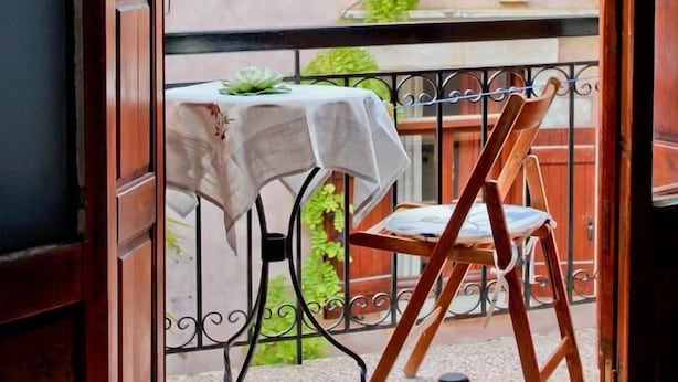 A balcony with a table and chair, a bed, and a view of a building with a balcony. - Smaragdi Rooms for Rent (Chania)