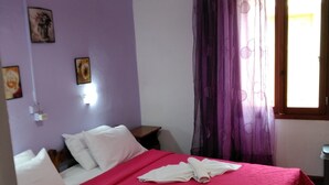 A room with a bed, a nightstand, a lamp, and a window with curtains. - Smaragdi Rooms for Rent (Chania)