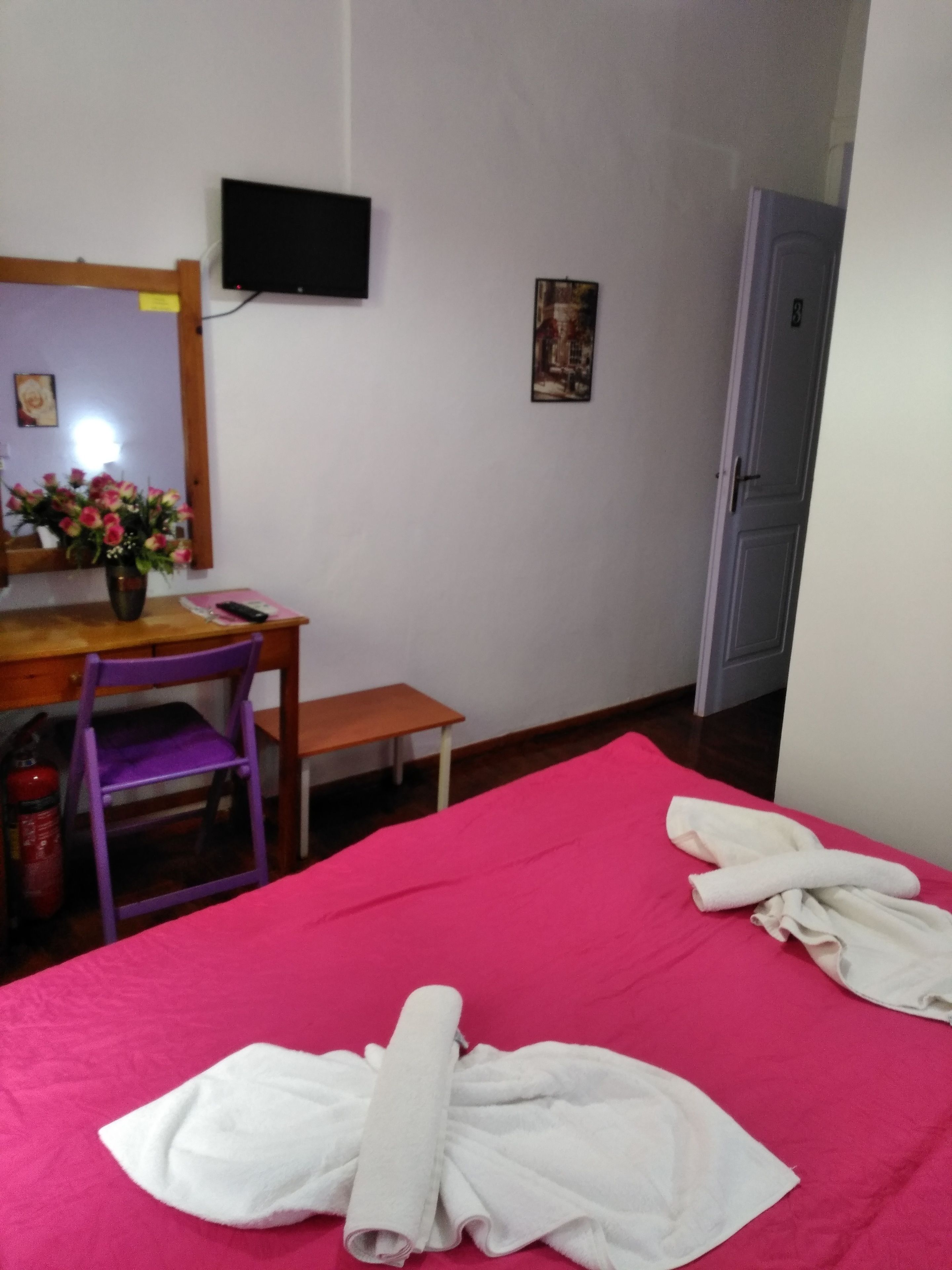 A room with a bed, a desk, a chair, a television, and a door.