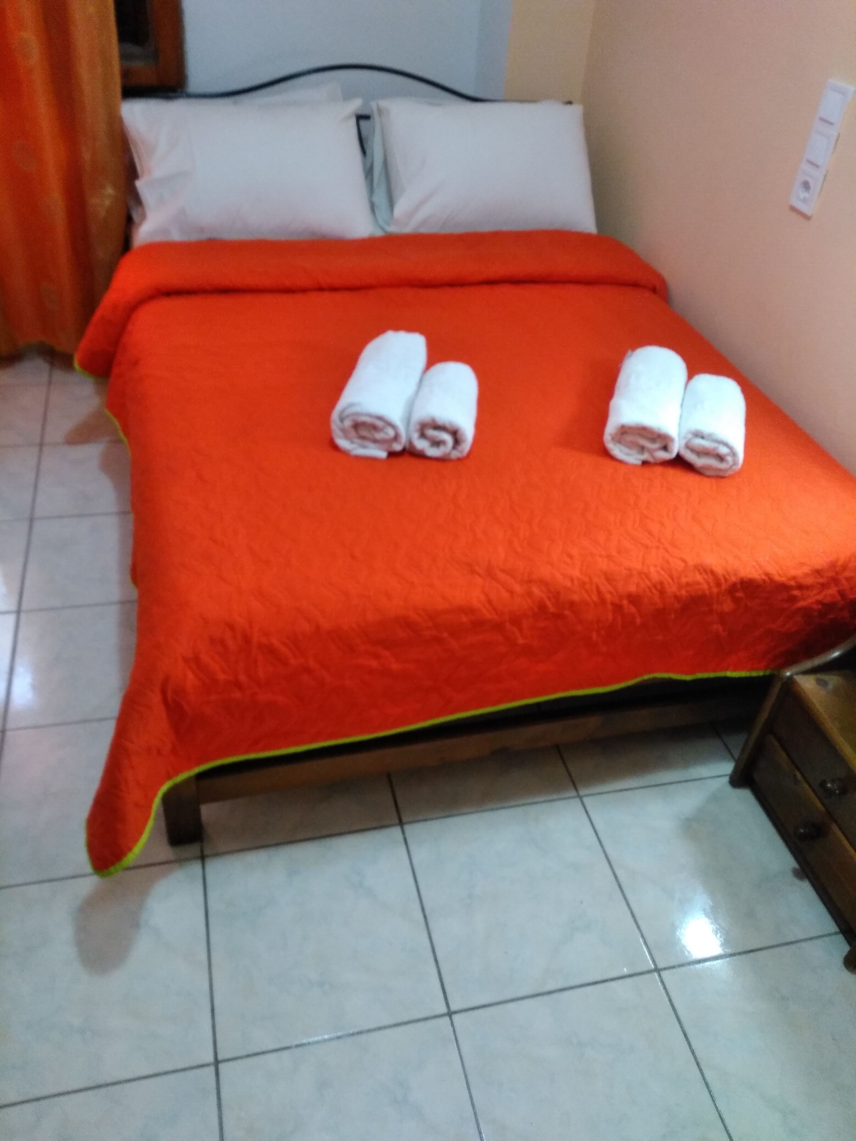 A bed with an orange bedspread and two rolled towels on it.