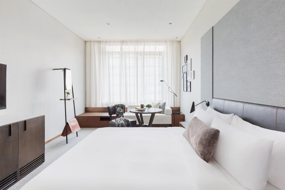 Una habitación de hotel moderna con una cama grande, una zona de estar con una mesa y un televisor a la izquierda.