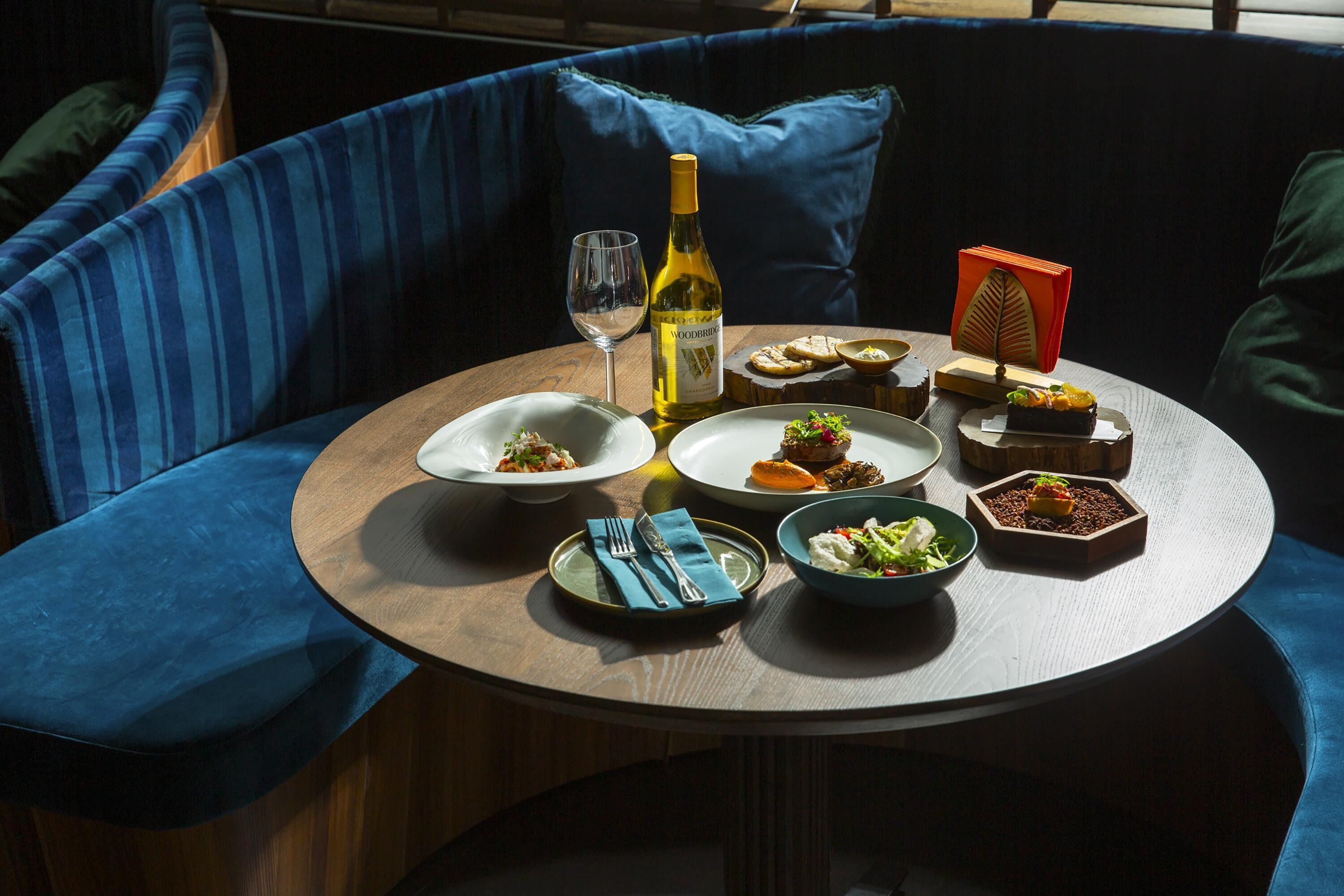 A round table with plates of food, a bottle of wine, and a glass of wine.