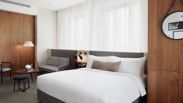 Una camera d'albergo con un letto grande, un divano grigio, un tavolino rotondo, una lampada e un pannello decorativo in legno.
