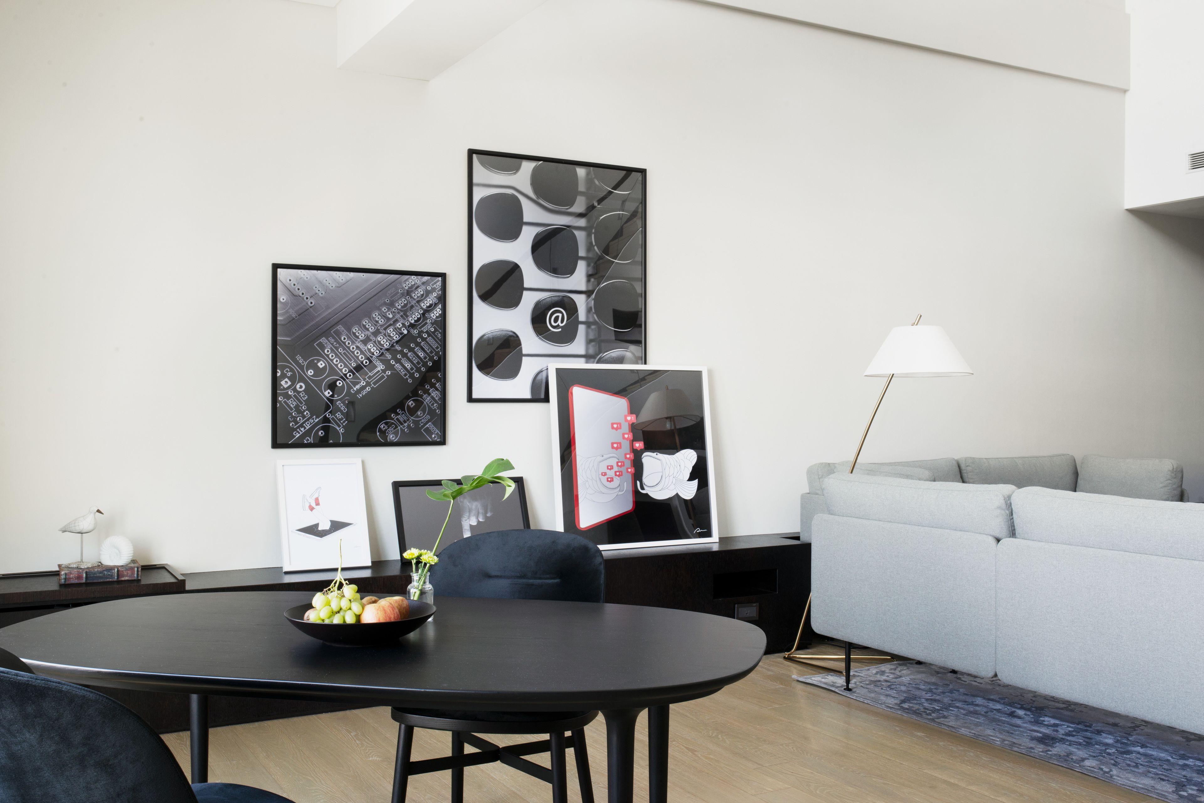 A modern living room with a round dining table, a grey sofa, and artwork on the walls.