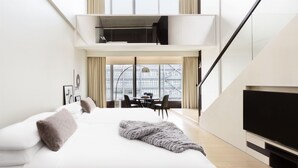 Een moderne hotelkamer met een groot bed, een flatscreen-televisie en een eethoek met uitzicht op de stad.