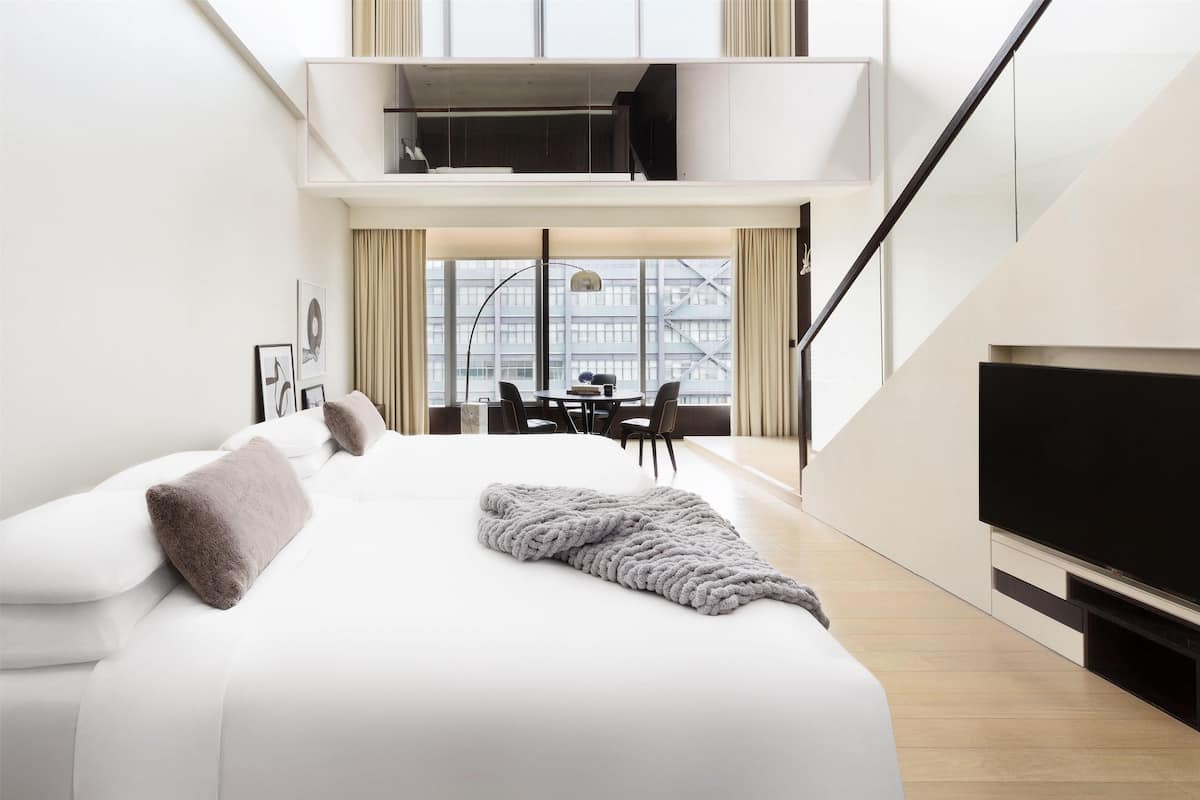 Habitación de hotel moderna con una cama grande, televisor de pantalla plana y zona de comedor con vistas a la ciudad.