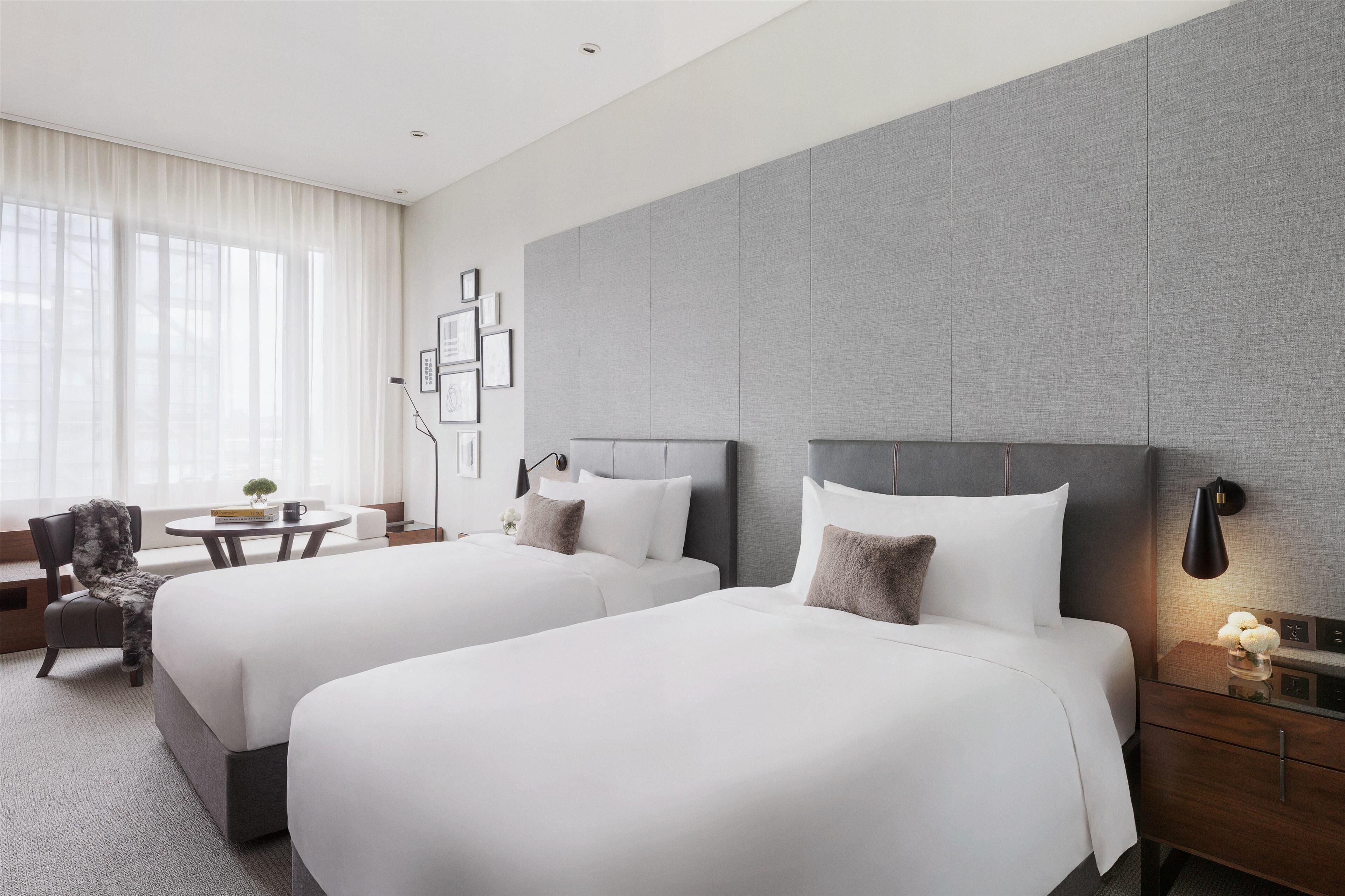 A hotel room with two beds, a desk, a chair, and a large window with curtains.